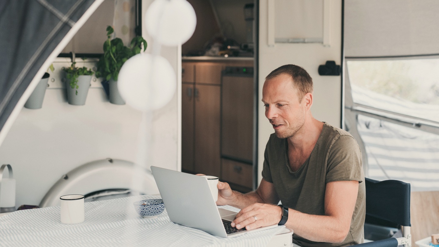 Image of a man drinking coffee while using his computer outside his RV