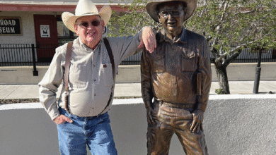 Historian and author Jim Hinckley poses next to a statue in Kingman, Ariz., honoring his contributions to preserving road trip adventures.